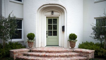 A warm white home exterior with a soft green front door in an arched doorway. 