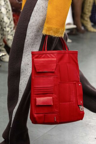 A closeup of a red Tory Burch cargo tote with exterior card slots and flap pockets.