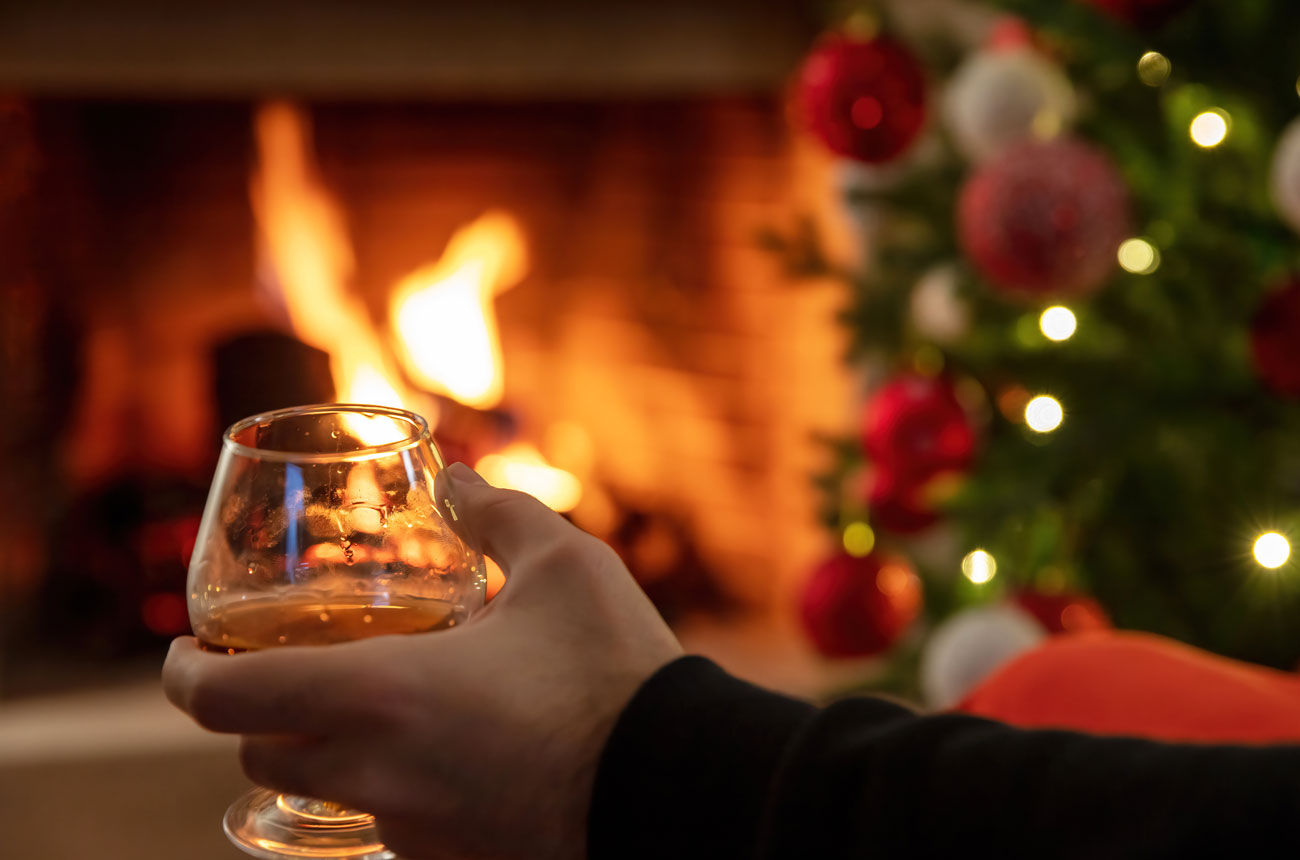 Hand holding a glass of Cognac with Christmas tree in background