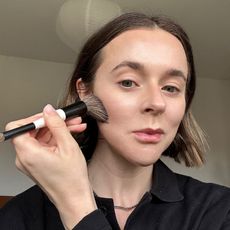A selfie of Grace Day using a makeup brush to apply a Trinny London bronzer to her cheeks
