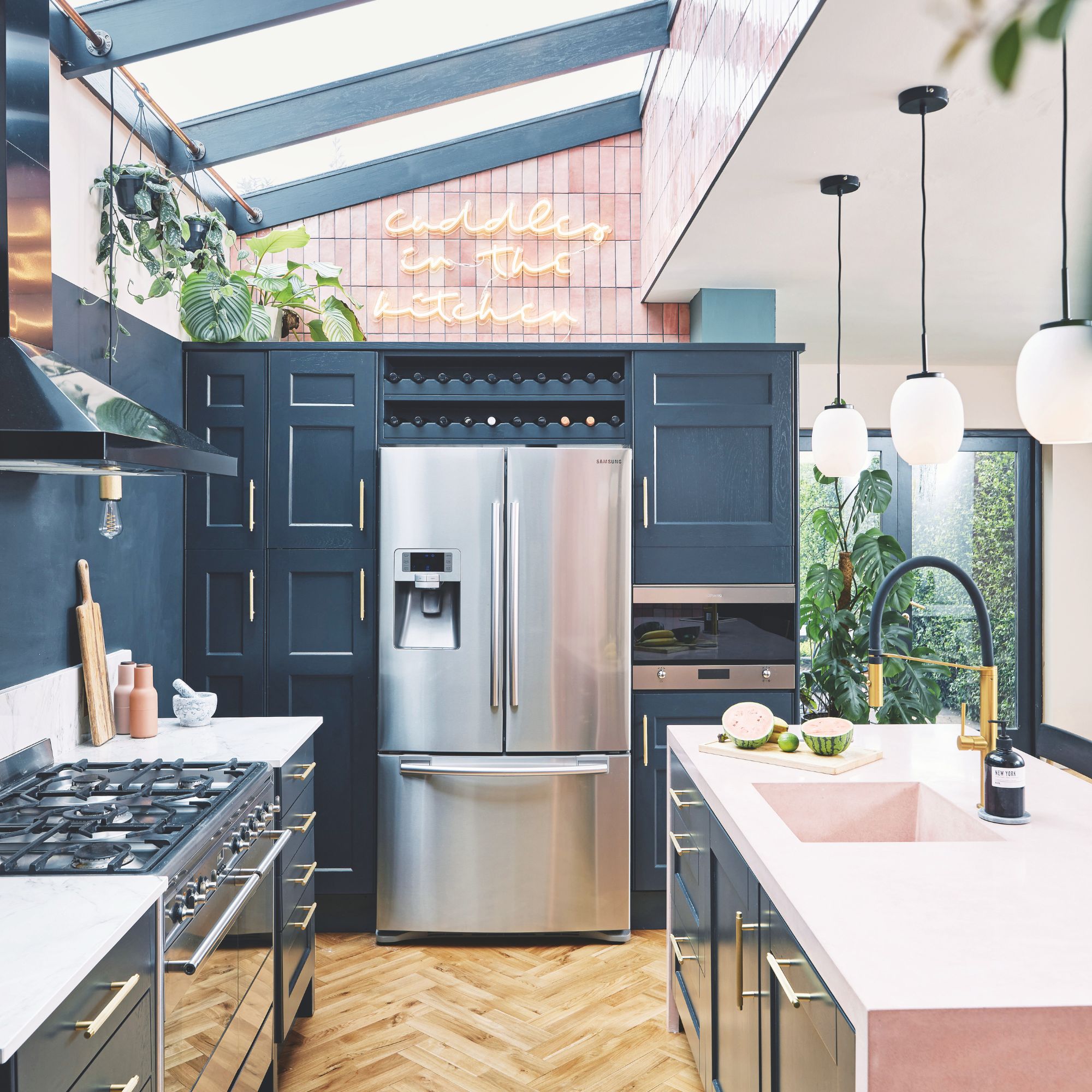 Kitchen with blue cabinets, wooden floors and a white worktop. A large fridge-freezer sits at the end of the kitchen