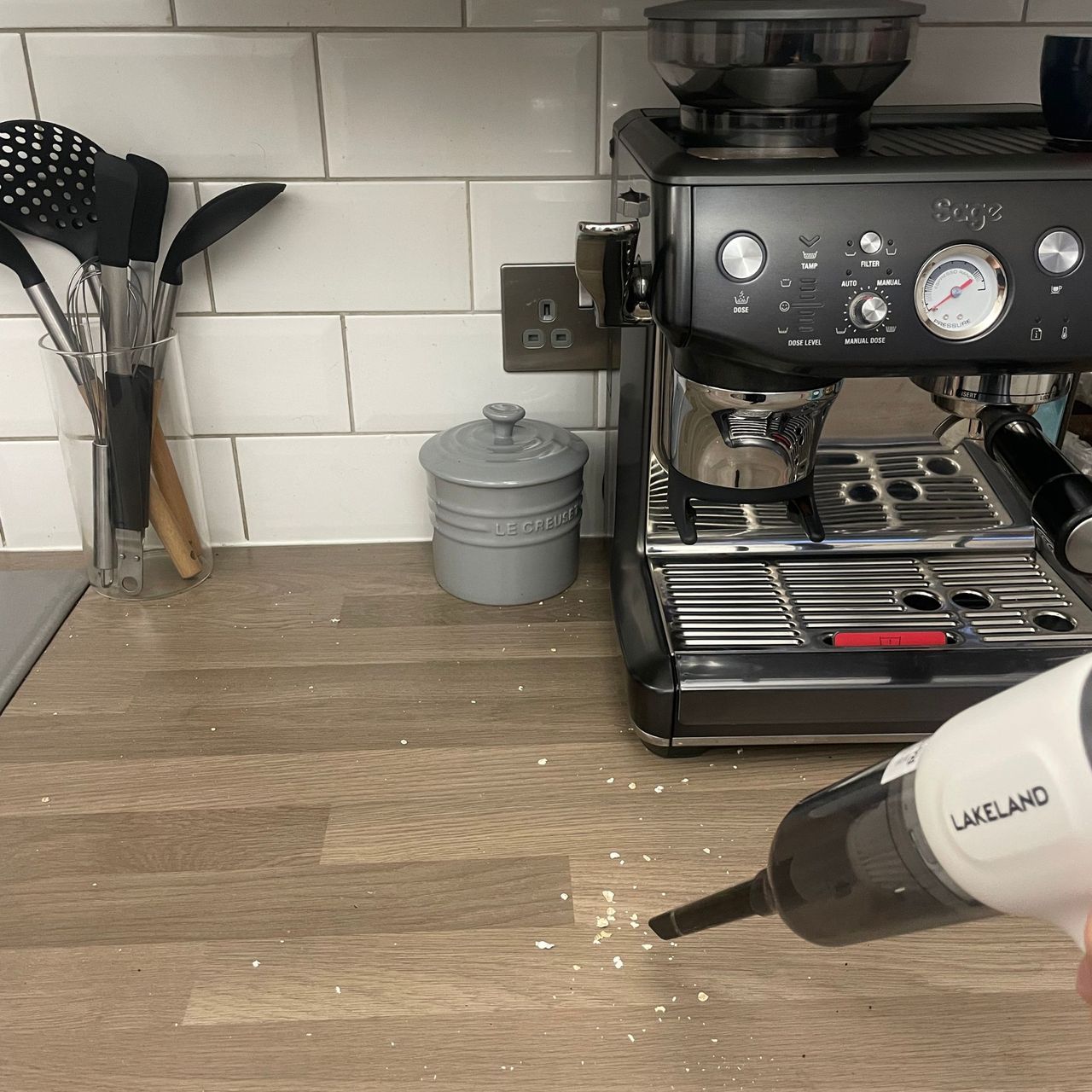 Using the Lakeland 3-in-1 Mini Vacuum Cleaner to clean kitchen counters, with a Sage coffee machine and utensils in the background