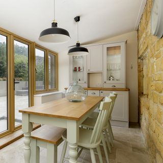 Cotswold stone cottage's dining room with brick wall, large glass windows and dining room table