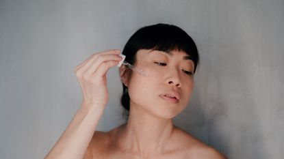 Woman with dark hair and short fringe applying the best serum for oily skin to her face