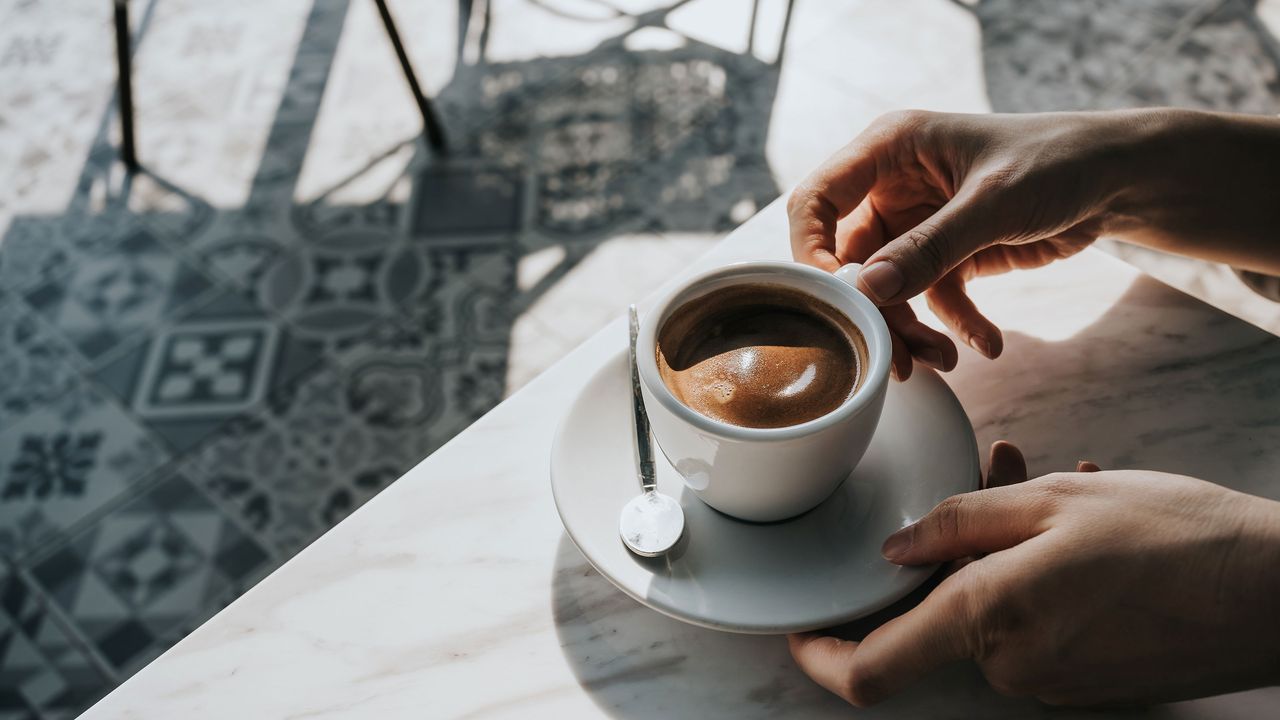 A woman enjoying an espresso coffee drink in white ceramic cup on patio