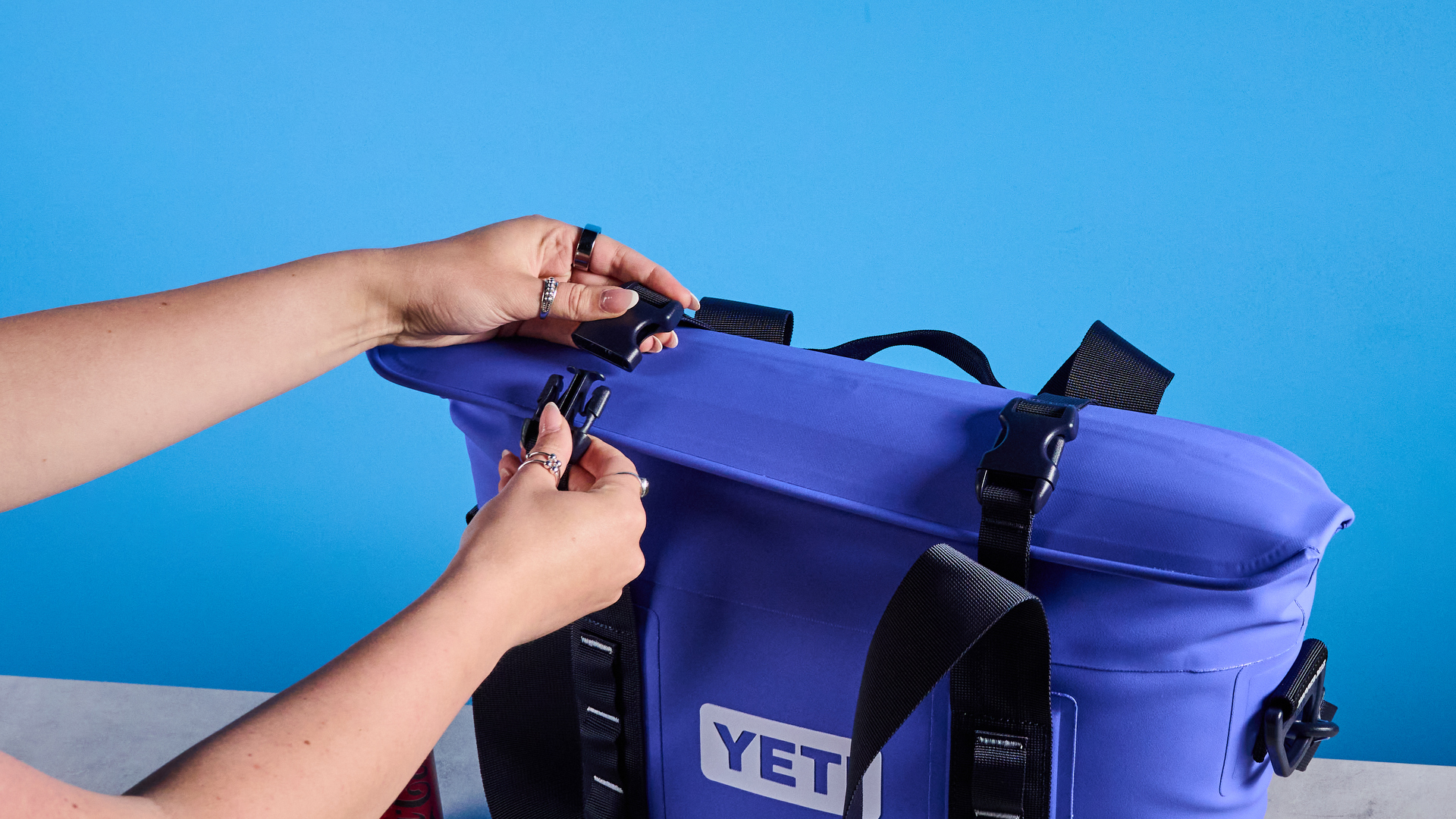 the yeti hopper m15 cool bag with a padded carry strap, handles, and a 15 quart capacity photographed with coke zero cans against a blue background