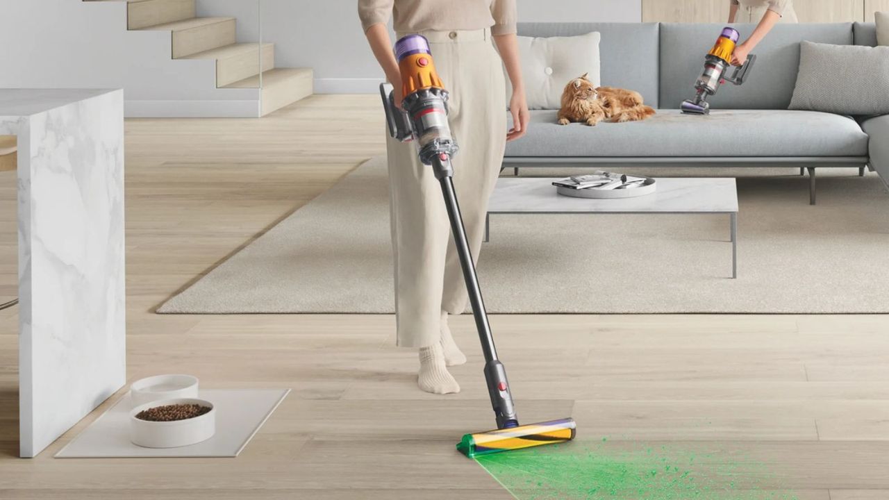 Image of person vacuuming hard floor with the Dyson V12 Detect Slim with somebody behind using the same vacuum in handheld mode next to a cat