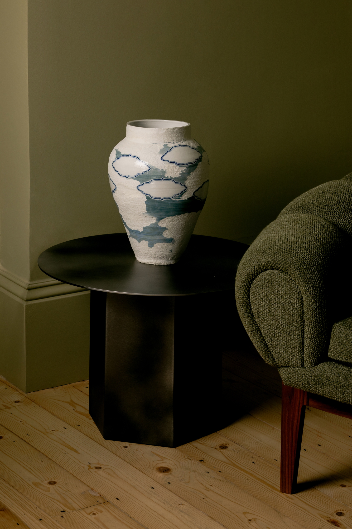A beautiful porcelain vase on a table next to a green chair