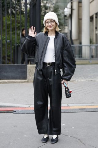 Gigi Hadid wears white top, black leather jacket, black leather pants, black ballet shoes, white beanie, black Miu Miu bag, outside Miu Miu, during the Womenswear Fall/Winter 2025/2026 as part of Paris Fashion Week on March 11, 2025 in Paris, France.