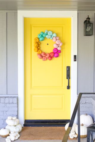 Yellow front door on porch decorated with multicolored pumpkin wreath