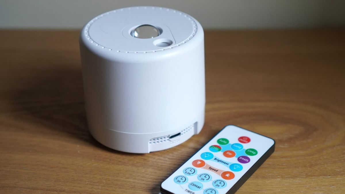 A white spherical projector is next to a multicolor remote control, both on a brown wooden surface.