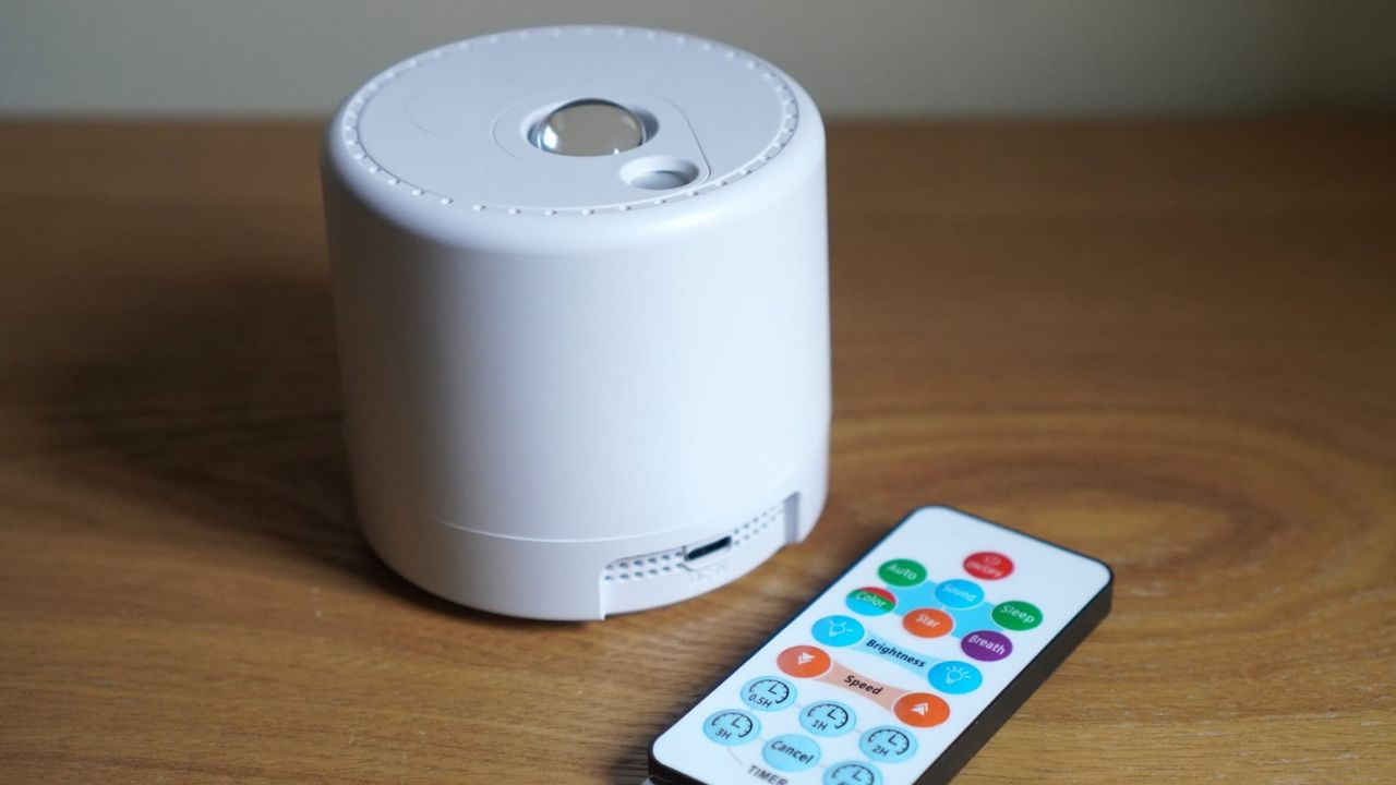 A white spherical projector is next to a multicolor remote control, both on a brown wooden surface.