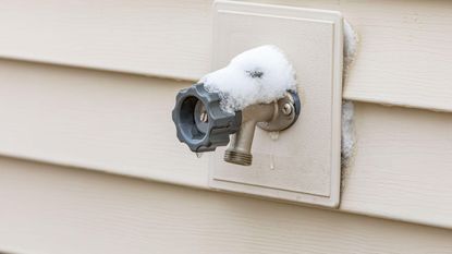 An outside faucet on the side of a house covered in frost