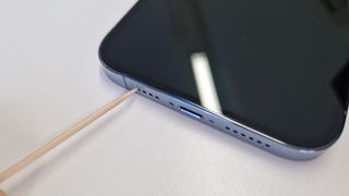 An iPhone 13 Pro Max's speakers being cleaned with a toothpick