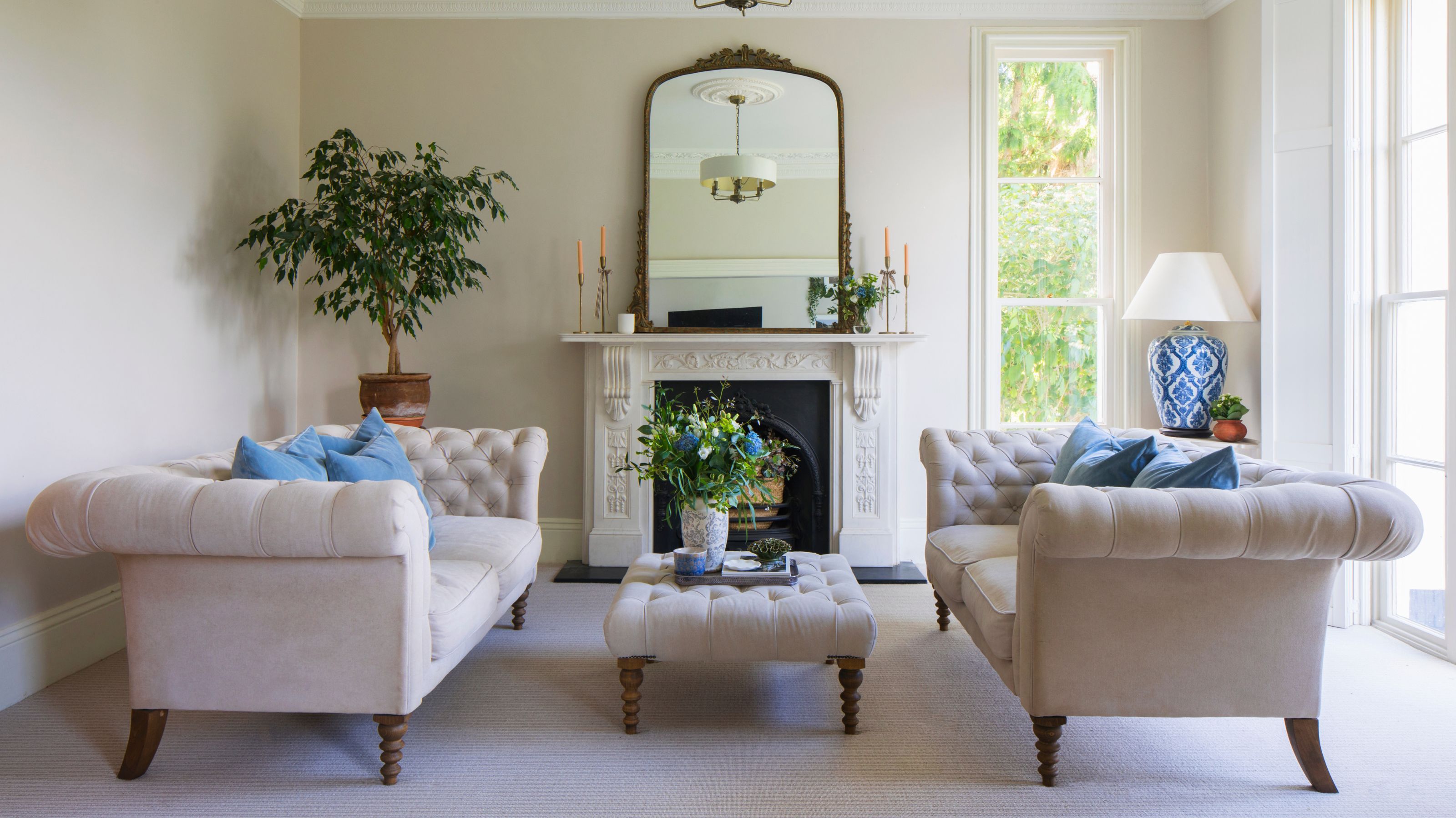Cream living room with two cream sofas separated by a matching coffee table, and a fireplace with a mirror on top of it