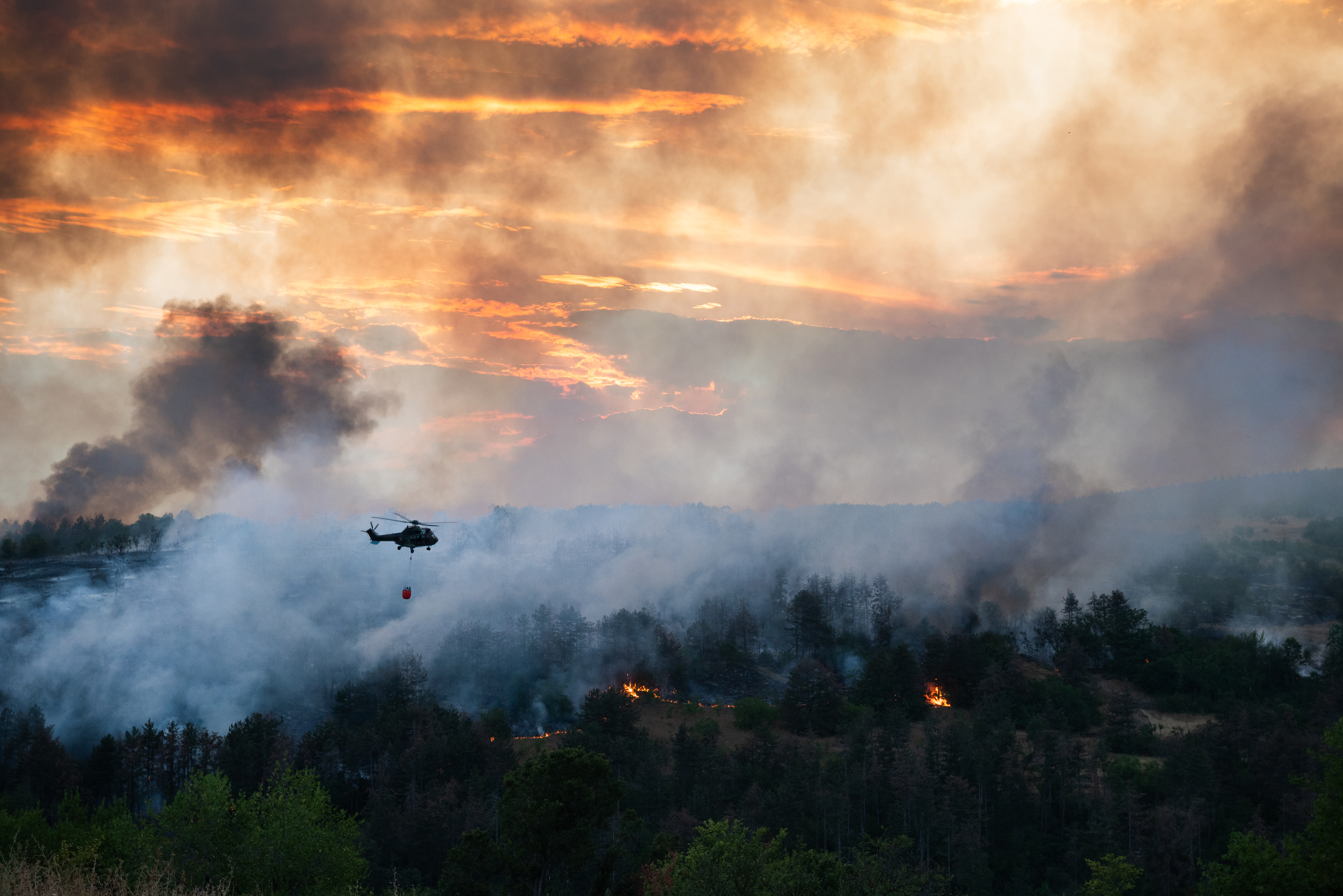 A photograph of a helicopter dropping water on a wildfire in Bulgaria.