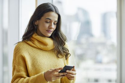 woman holding a smart phone - how to download new NHS track and trace app