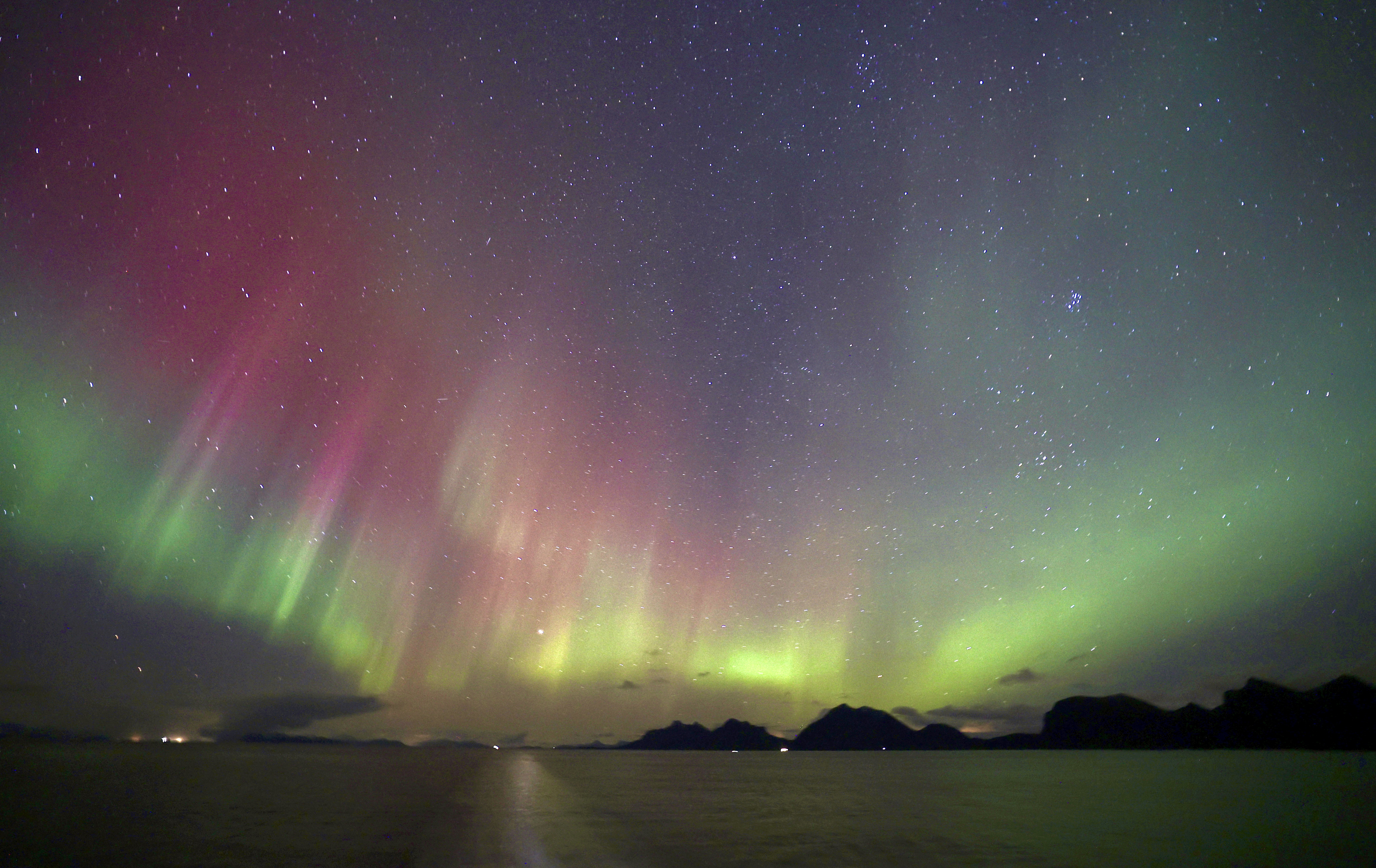 sweeping green northern lights appear as ribbons in the sky reflected in the water below