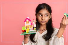A girl holding up a LEGO creation against a pink background