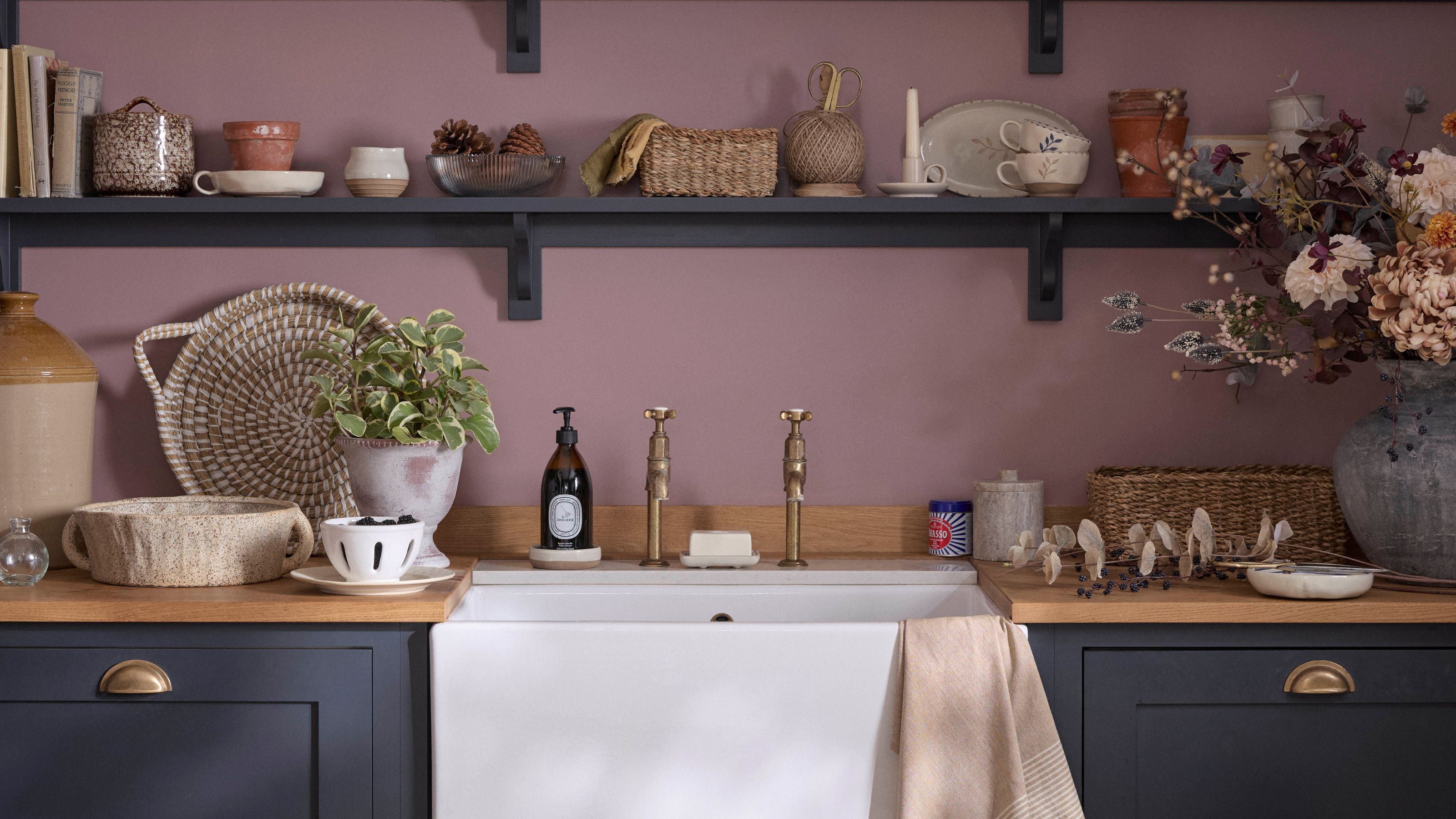 A purple laundry room with dark navy shelving and cabinets, and a large white sink with gold faucets. On the shelves are trays, trinkets, and a large grey vase.