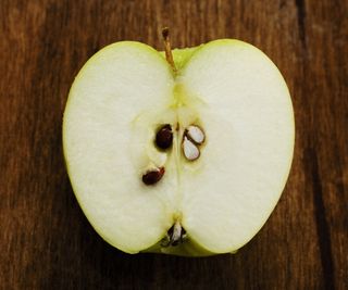 An apple cut in half on a wooden board to show the seeds inside