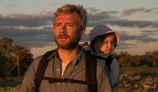 Cargo Martin Freeman with his baby on his back, watching the sunset