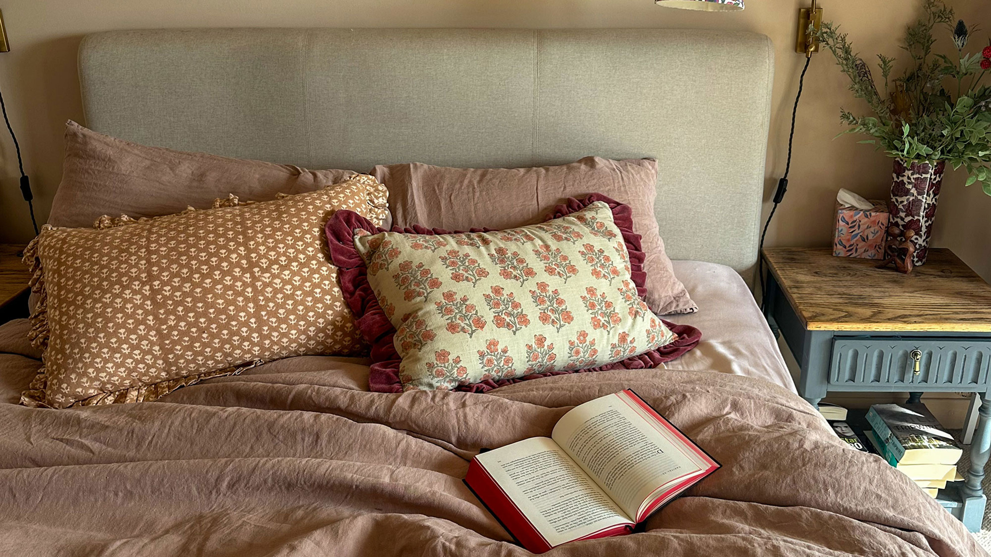 Bed with pink linen sheets, block pattern printed cushions, upholstered headboard and wooden bedside table