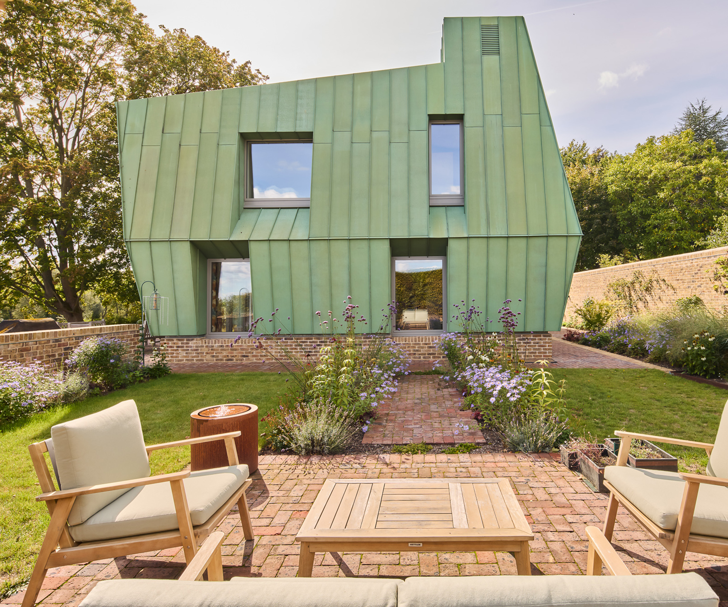 Exterior view of a copper clad self build project with a sunny patio in the front of the shot