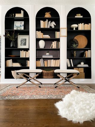 A living room with a wall of arched shelves decorated with books and with the inside of the shelves painted black