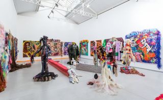 Art gallery with white walls, ceiling and grey flooring featuring 17 ballsy canvases, seven grotesque sculptures, seven additional patchwork dolls on knotted rope benches