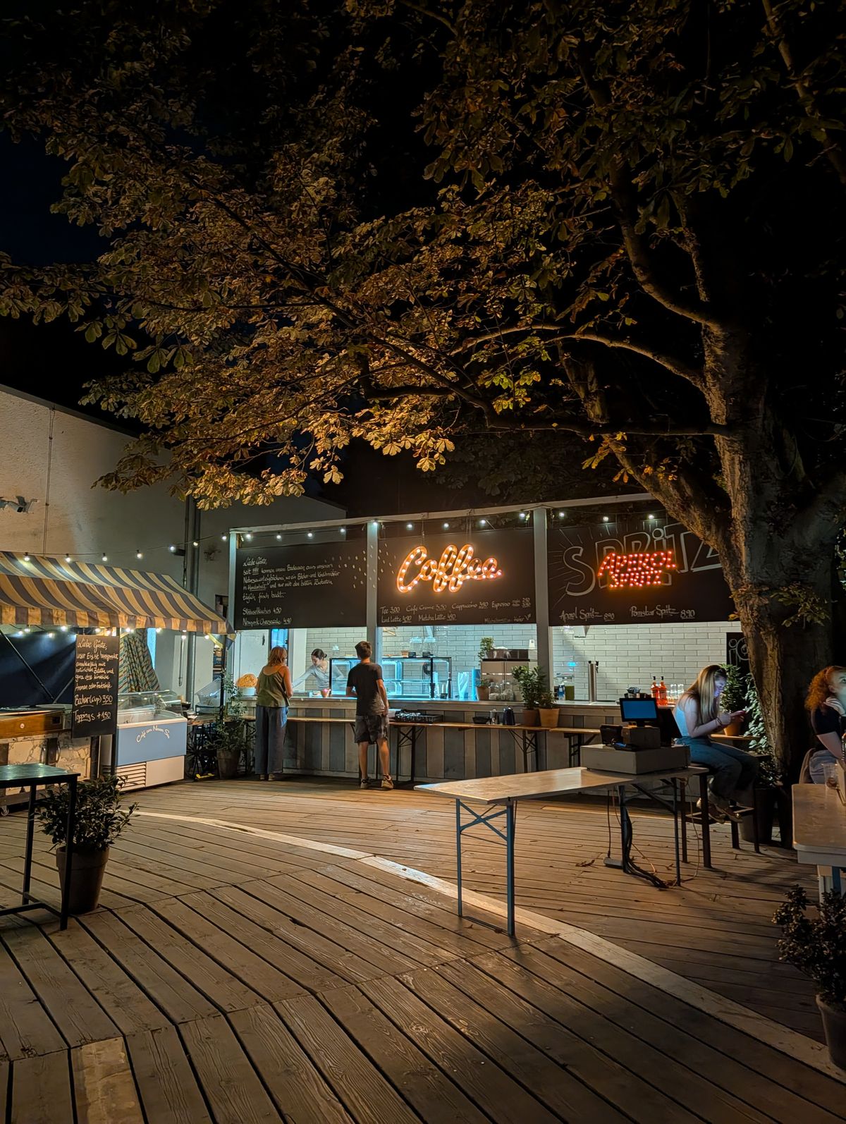 A bar with signs for coffee in Aprerol spritz lit up at night