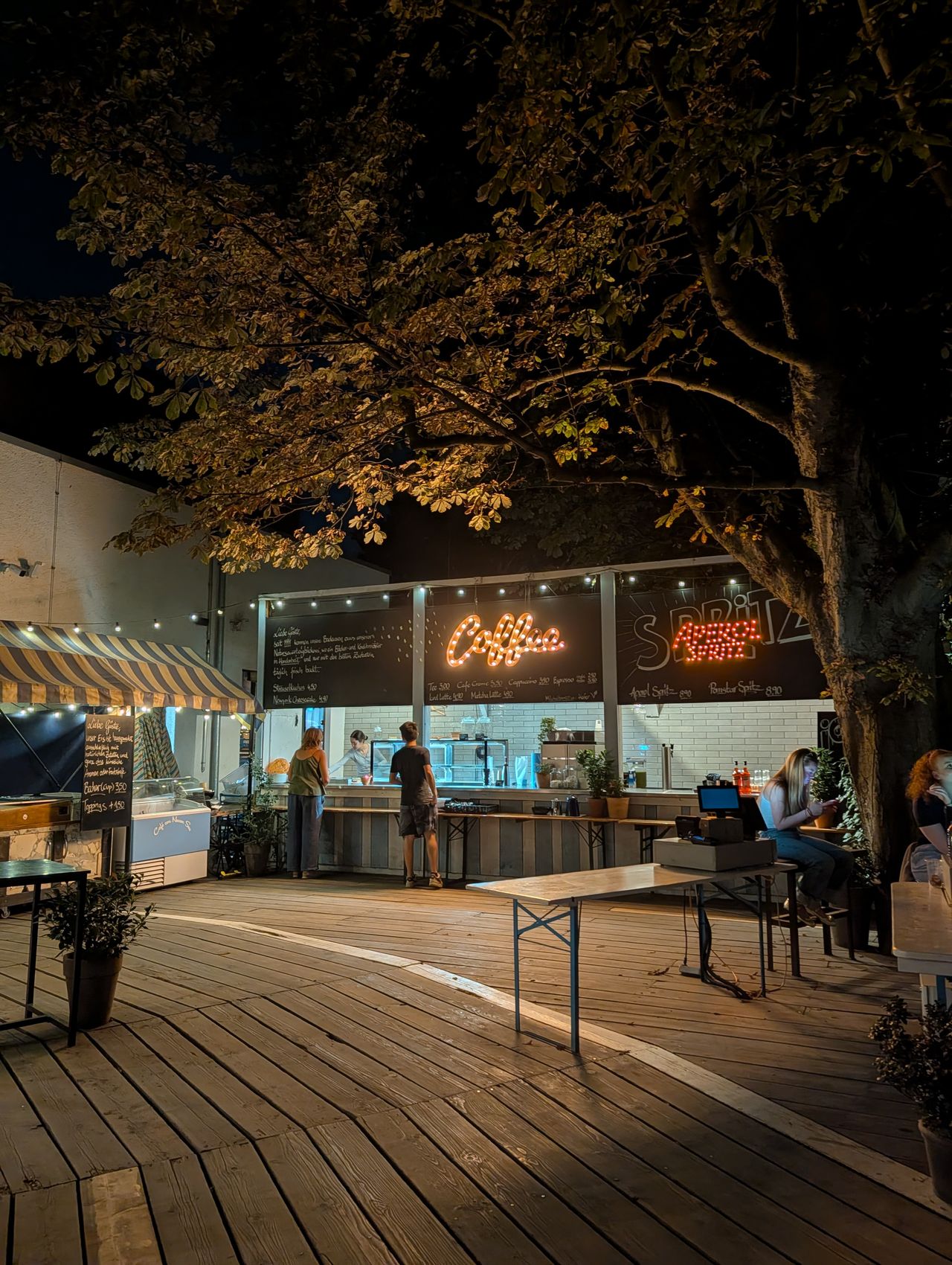 A bar with signs for coffee in Aprerol spritz lit up at night