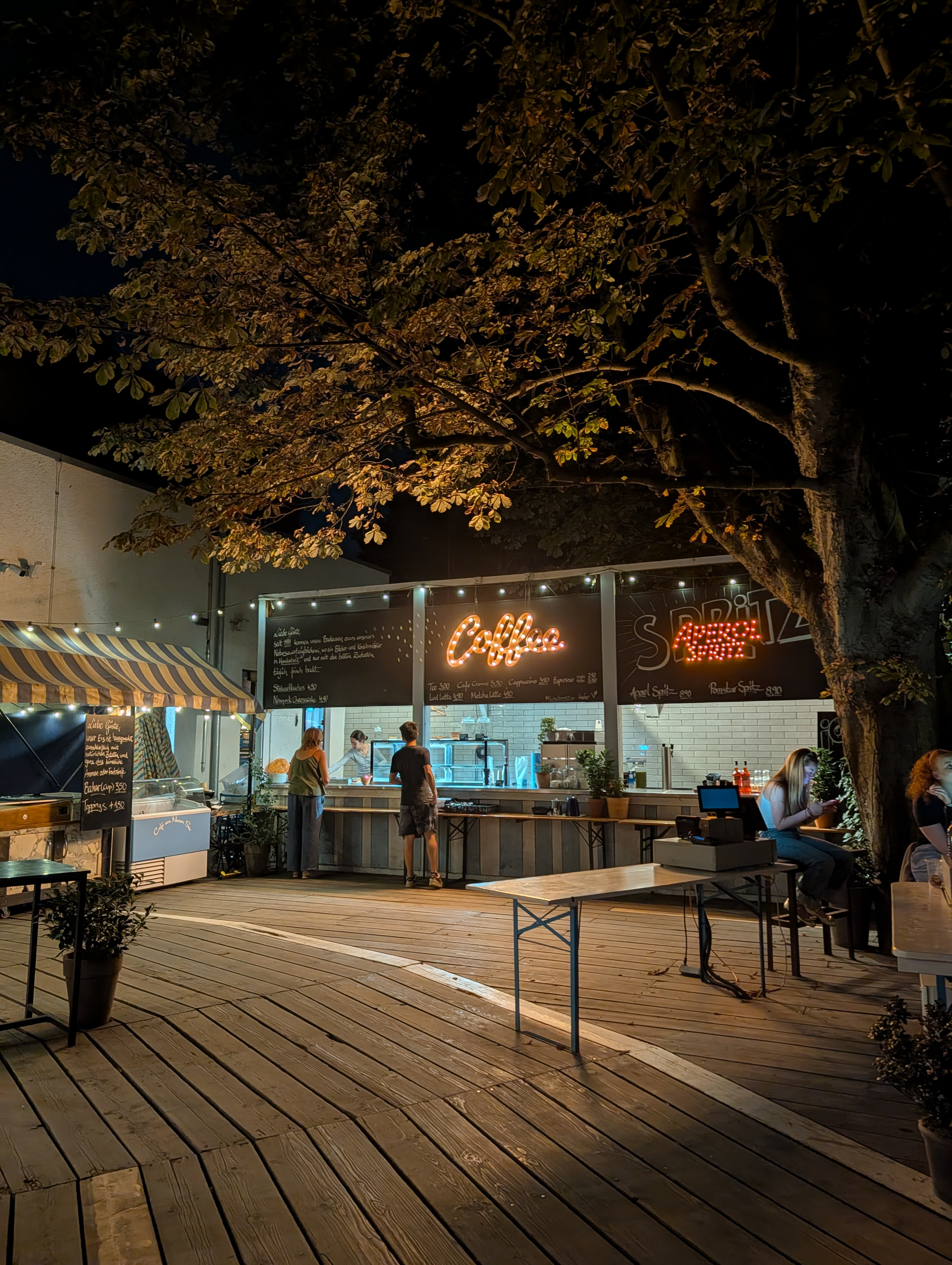 A bar with signs for coffee in Aprerol spritz lit up at night