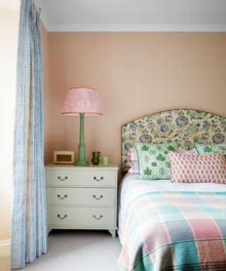 Pink bedroom, bed with colorful bedding, bedside table, colorful table lamp, patterned curtains, gray carpet