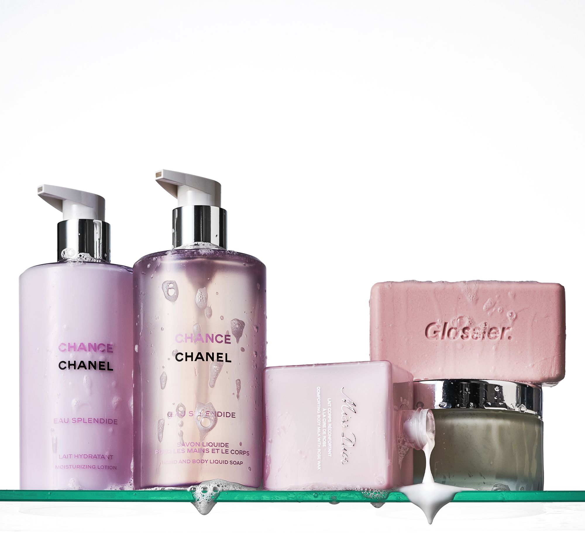 A picture of Chanel body lotion and cream, Dior body cream, Hermes body cream and Glossier soap on a shower shelf