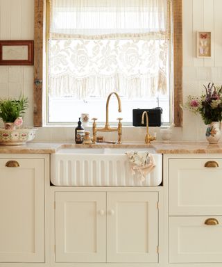 white kitchen with gold faucet, butler sink, brass hardware, net curtain, cottage style