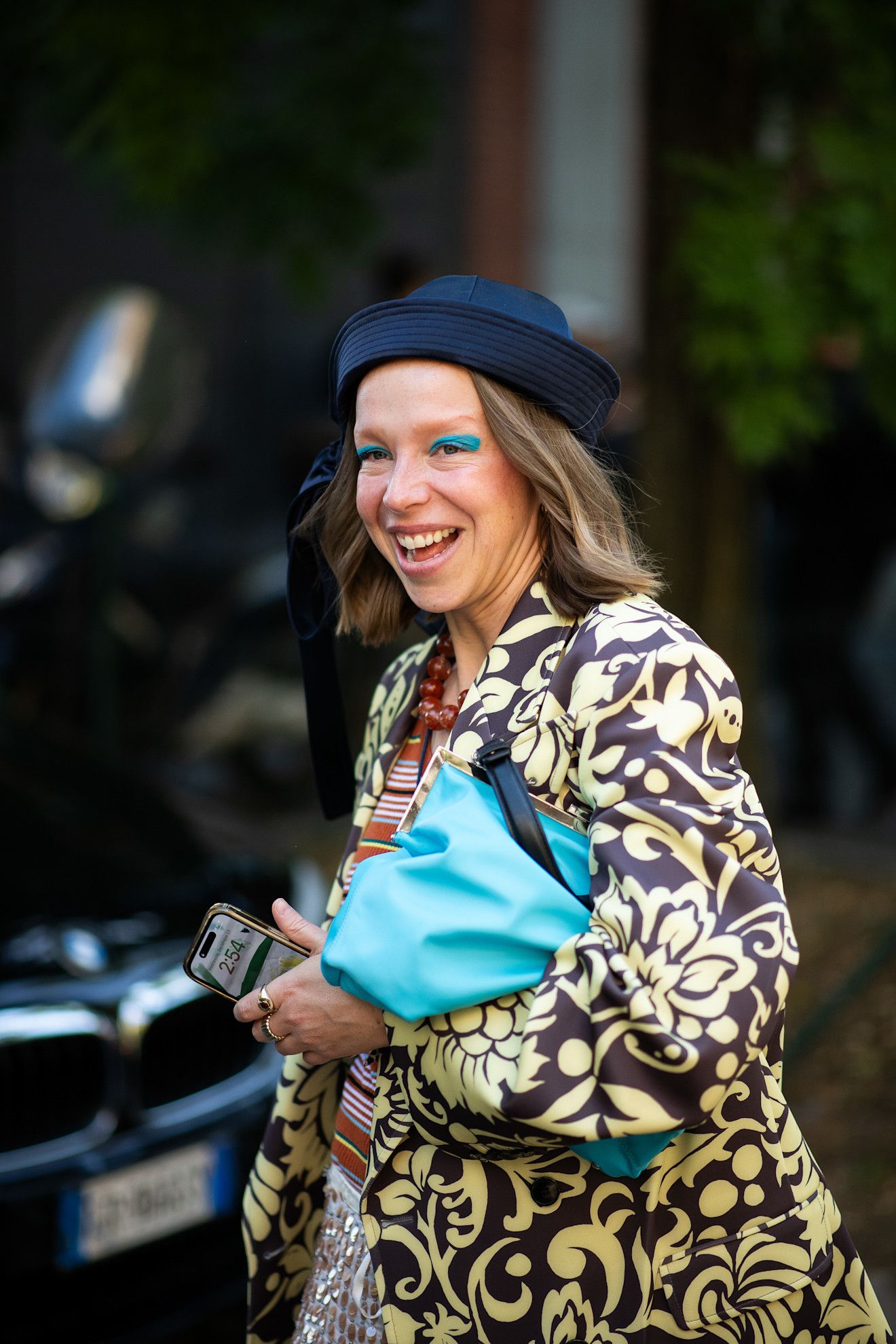 a white woman with a blonde bob and yellow coat with green eyeshadow
