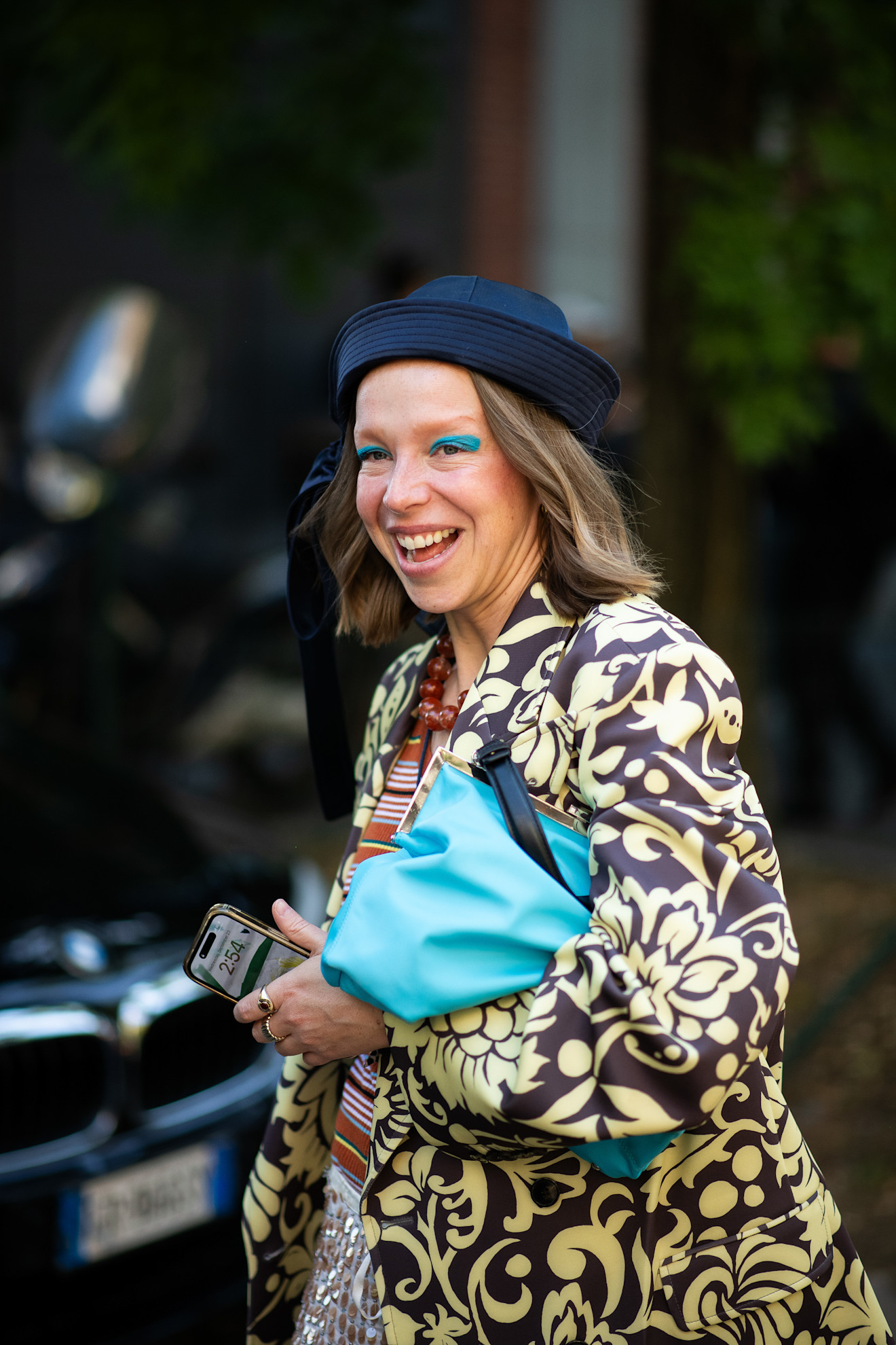 a white woman with a blonde bob and yellow coat with green eyeshadow