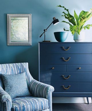 Dark blue chest of drawers, with a small armchair in the foreground against teal painted walls.