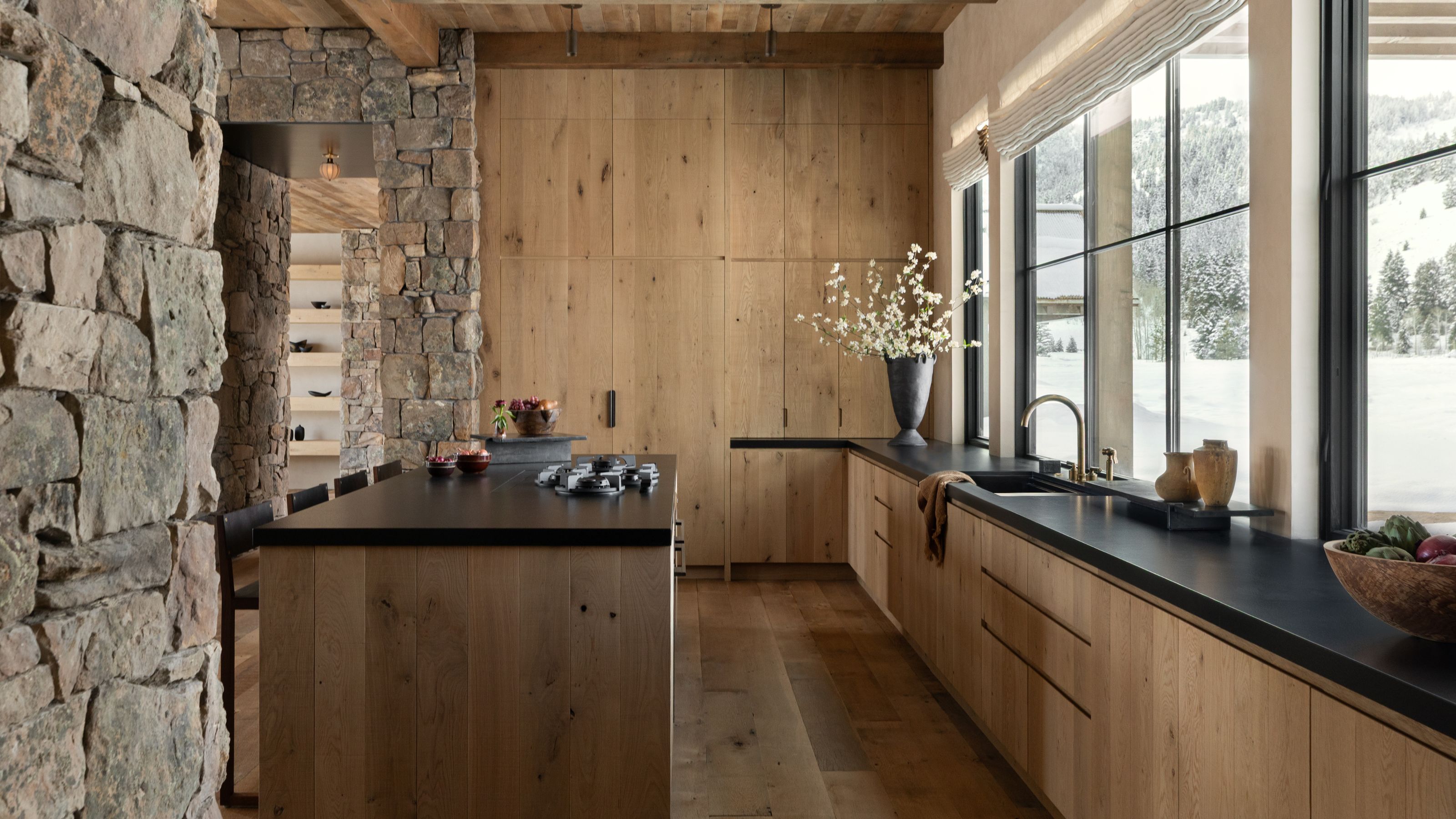 a mountain kitchen clad in warm oak cabinet panels with stone walls and black countertops