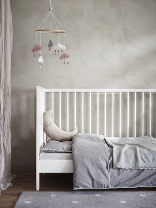 gray gender neutral nursery with white cot, gray bedding, gray textured walls and rug. Cloud wall hanging