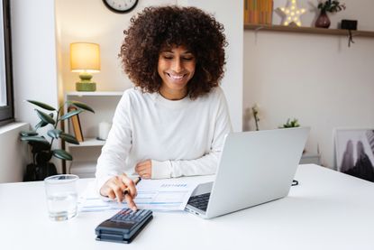 Young woman is smiling while using a calculator and laptop for her home finances