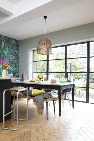 Dining area with herringbone floor, Crittall-style doors leading to decking, farmhouse table with black painted legs and wood top, and bench