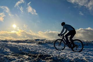 Man cycling on a snowy trail into the sun