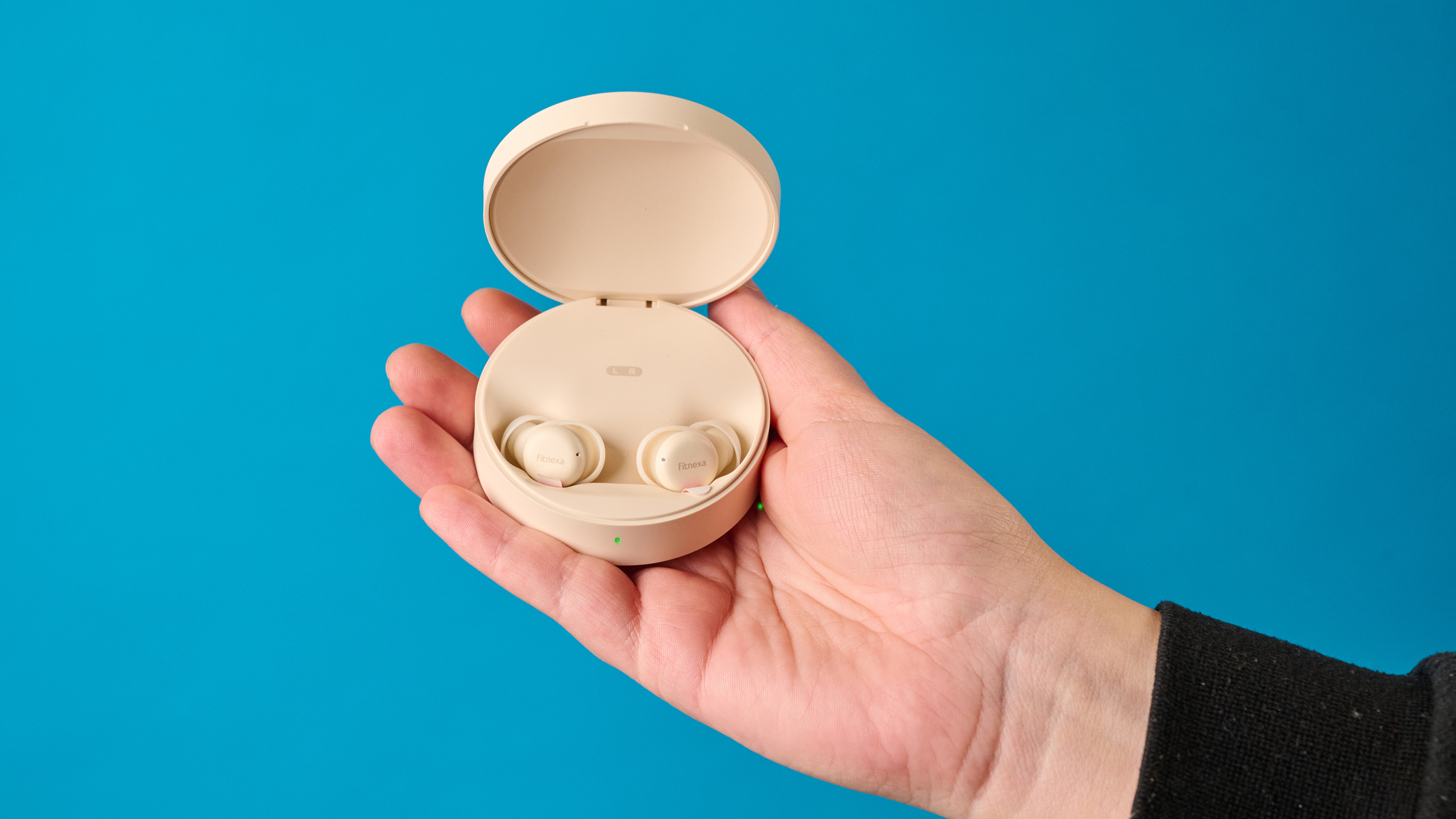 A close up of a hand holding the Fitnexa SomniPods 3 case with the lid open showing the ear buds inside, against a blue background