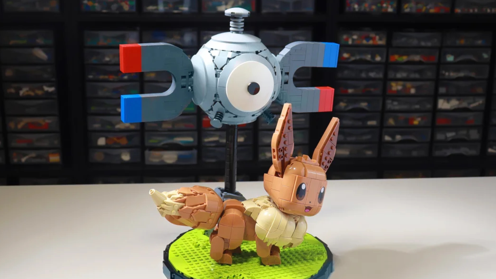 A fan-made Lego Magnemite above a Lego Eevee on a white table, with shelves of Lego pieces visible in the background