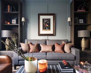 gray living room with gray sofa, orange cushions, gray panelling and dark wood shelves