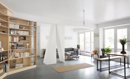 Interior of a loft space designed by Sophie Dries with white walls, wooden bookshelves , black flooring and grey and wooden furniture