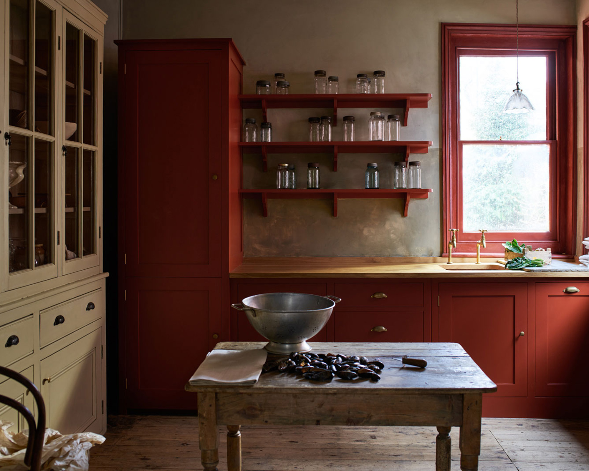 A rusty red kitchen cabinetry with raw wooden flooring and cream dresser