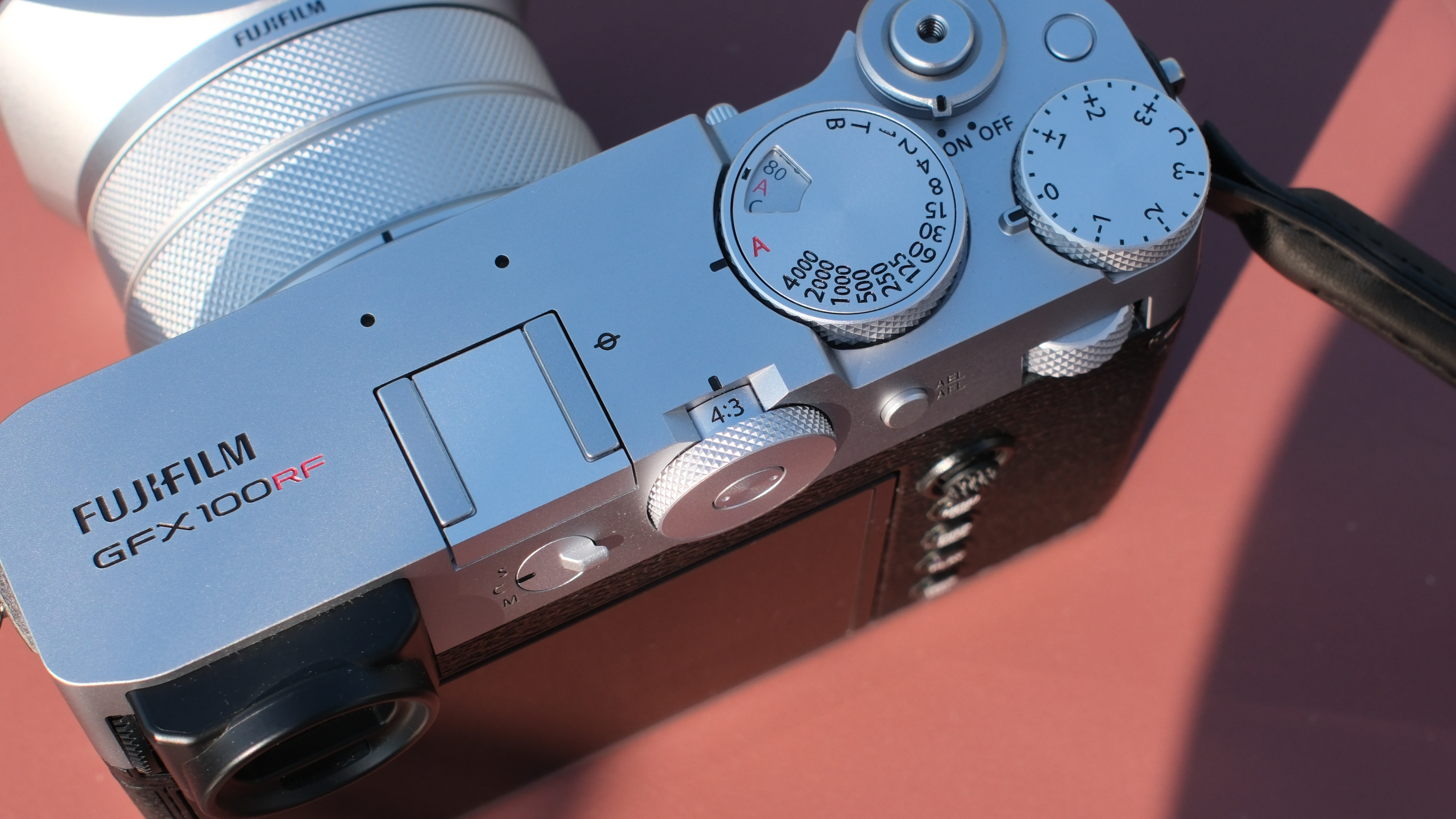 Close-up of the Fujifilm GFX 100RF camera dials on a red table in bright sunlight